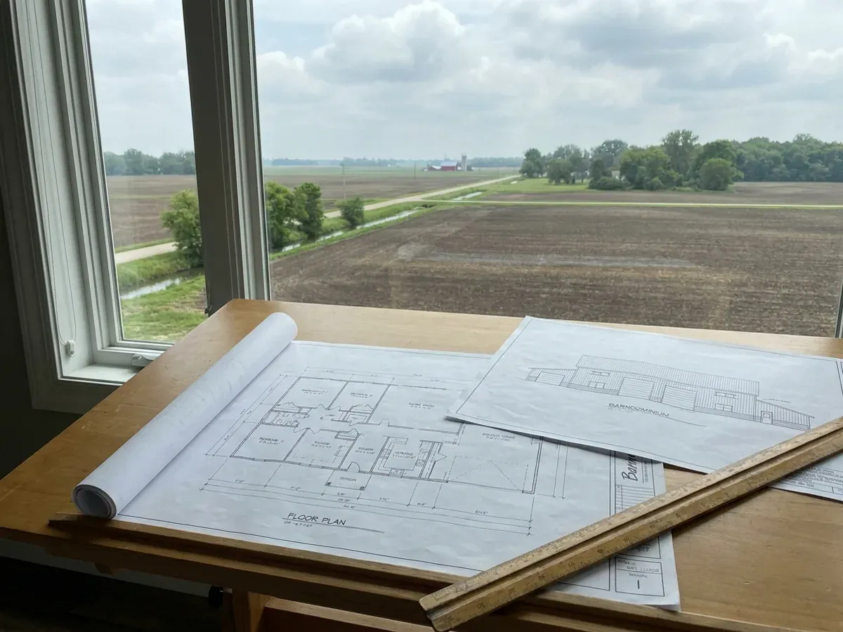 Barndominium floor plan and elevation drawings laid out on a drafting table with a scale rule.