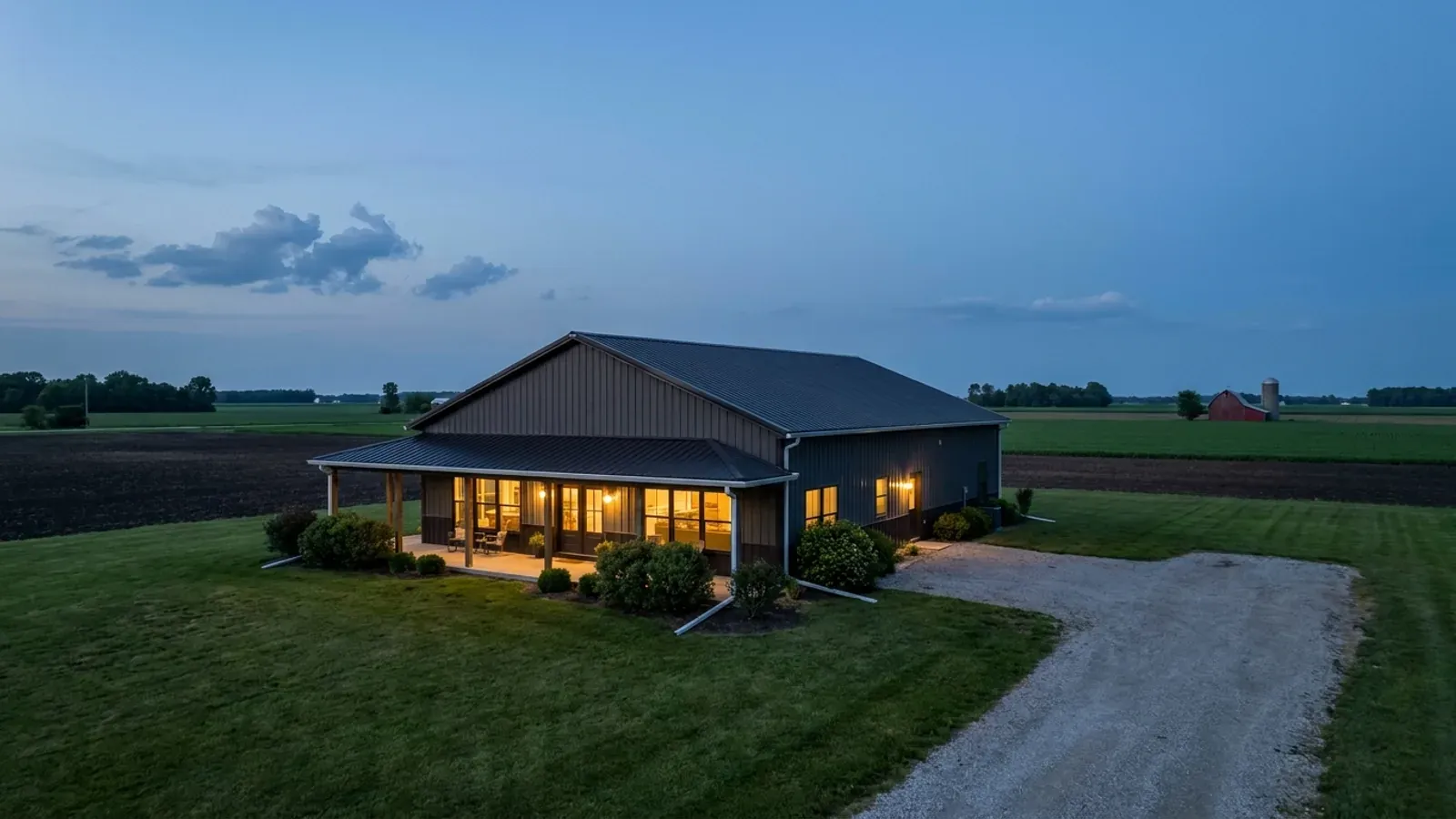 A finished barndominium at dusk with warm interior lighting glowing through its large windows.